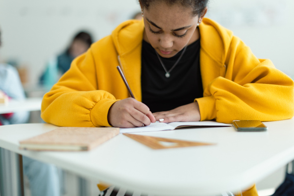 High school students paying attention in a class, sitting in their desks and writing notes, back to school concept.