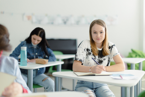 High school students paying attention in a class, sitting in their desks and writing notes, back to school concept.