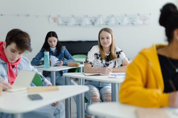 High school students paying attention in a class, sitting in their desks and writing notes, back to school concept.