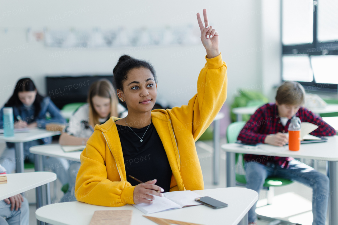 High school students paying attention in class, sitting in their desks and raising hands.