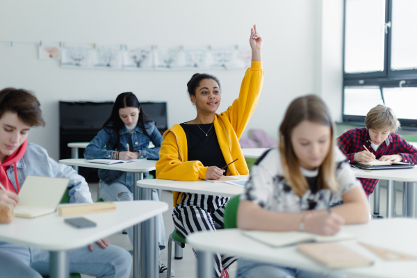 High school students paying attention in class, sitting in their desks and raising hands.