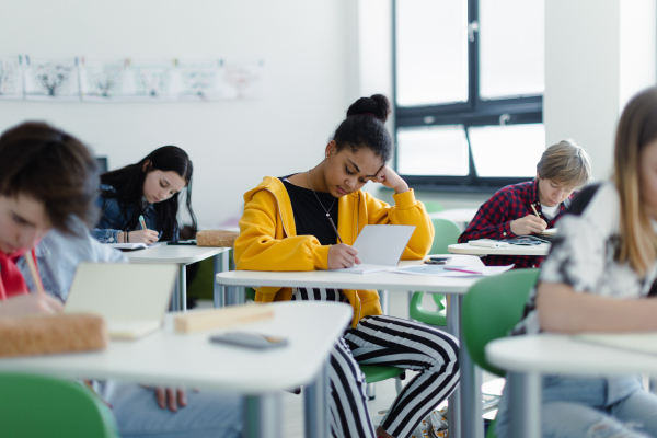 High school tired students writing notes in a class, sitting in their desks, back to school concept.