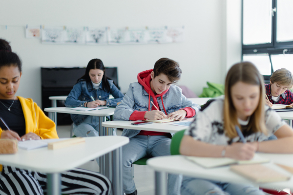 High school students paying attention in a class, sitting in their desks and writing notes, back to school concept.