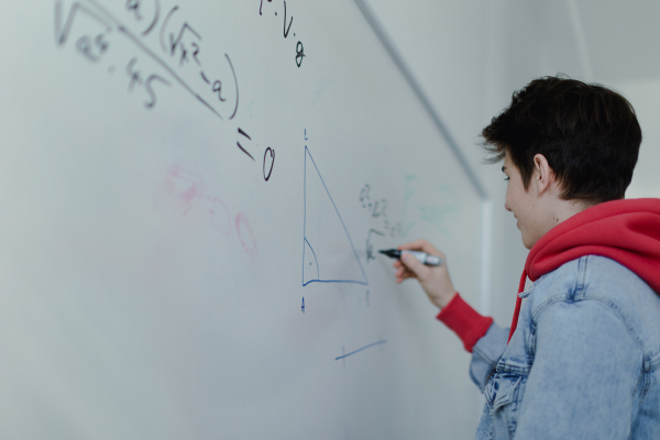 A back view of high school student solving math problem on whiteboard in classroom.