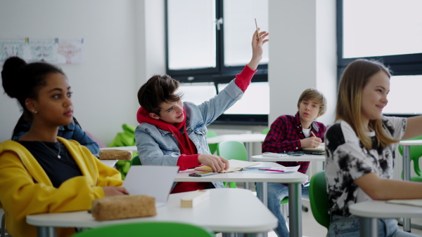 High school students paying attention in class, sitting in their desks and raising hands.