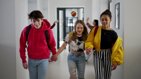 Young high school students holding hands and walking in a corridor and looking at camera at school.