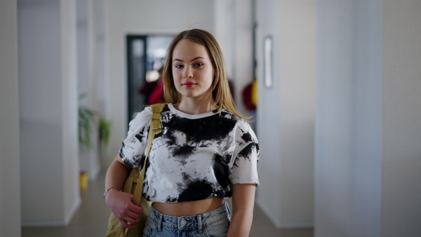 A young high school student girl standing in corridor and looking at camera at school.