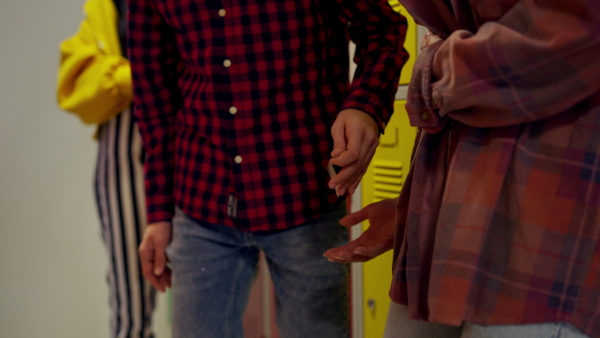 Unrecognizable high school students dealing drugs in a shool corridor.