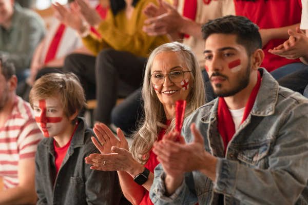 Excited football fans supproting an English national team in live soccer match at stadium.