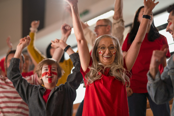 Excited football fans supproting an English national team in live soccer match at stadium.