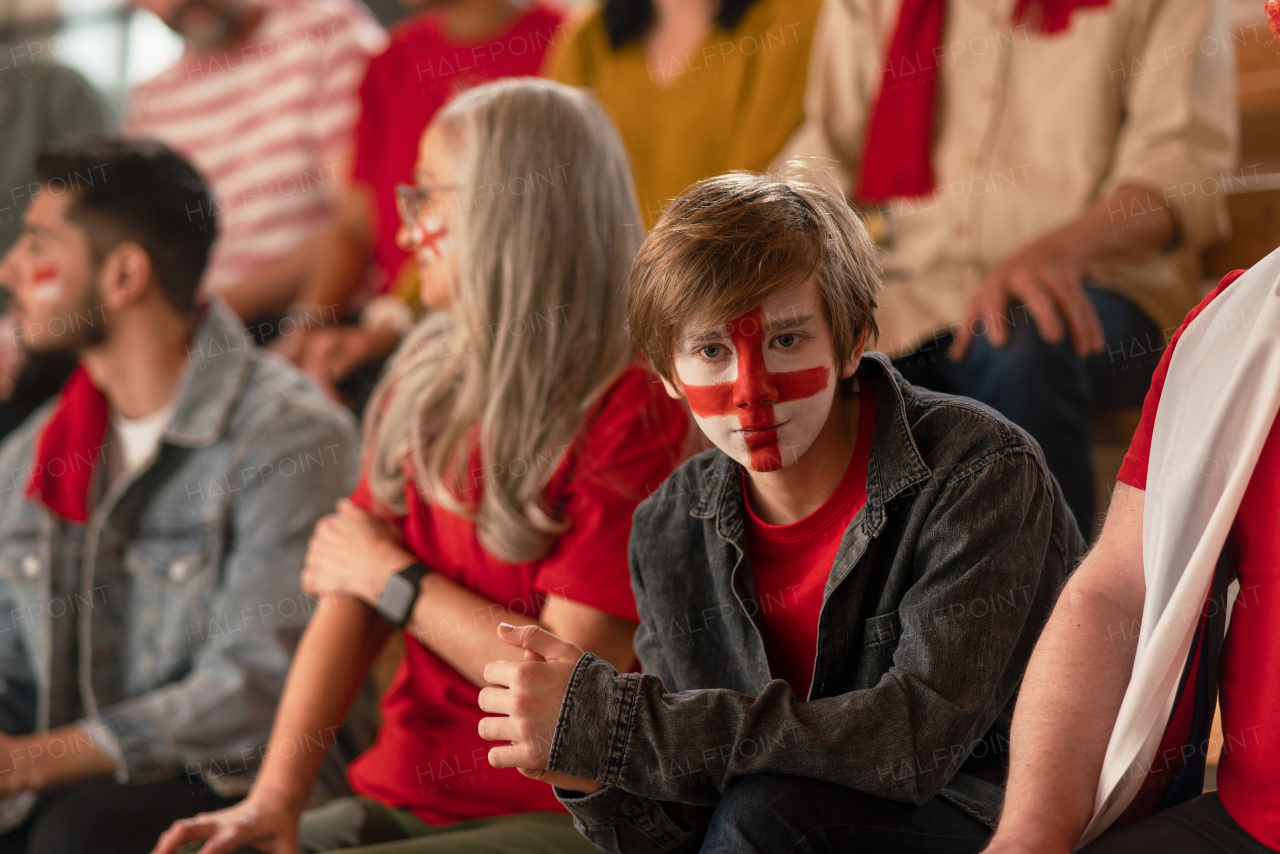 An excited football fans supporting English national team in live soccer match at stadium.