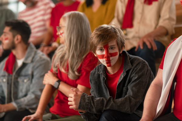 An excited football fans supporting English national team in live soccer match at stadium.