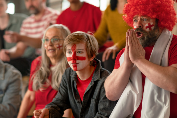 Excited football fans supproting an English national team in live soccer match at stadium.