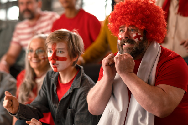 Excited football fans supproting an English national team in live soccer match at stadium.