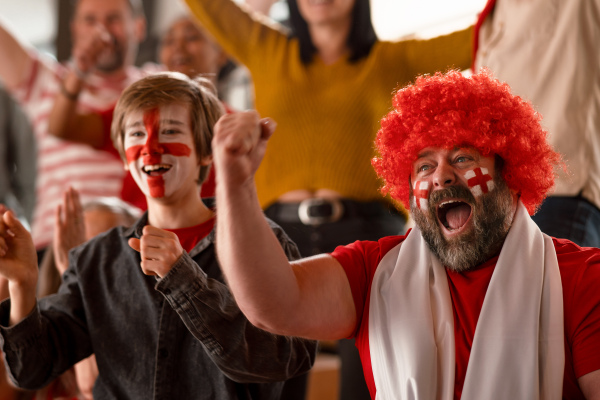 Excited football fans supproting an English national team in live soccer match at stadium.