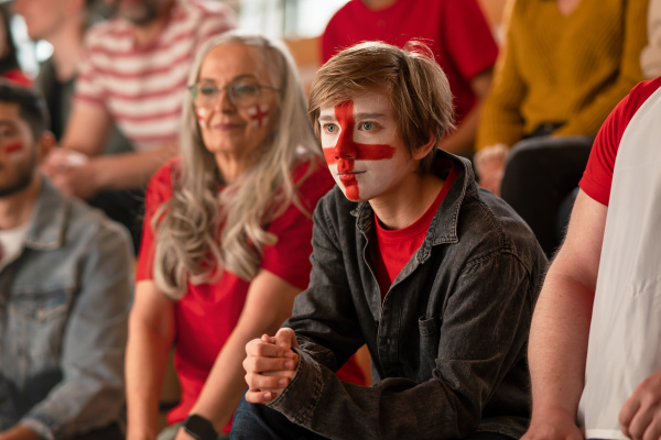 Excited football fans supproting an English national team in live soccer match at stadium.