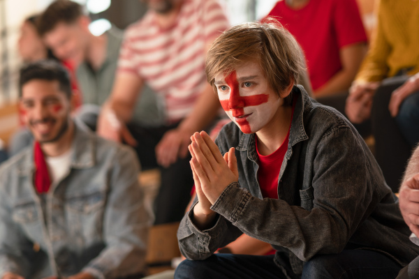 Excited football fans supproting an English national team in live soccer match at stadium.