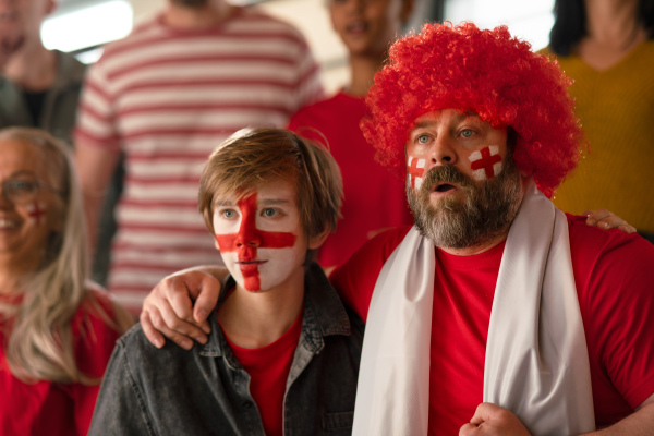 Excited football fans supproting an English national team in live soccer match at stadium.