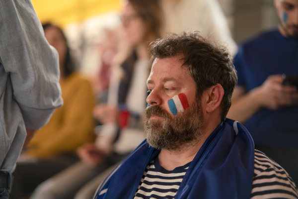 Worried football fans supporting a French national team in live soccer match at stadium.