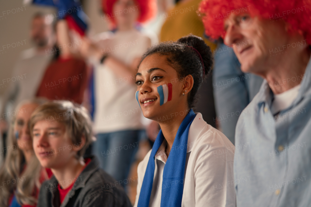 Excited football fans supproting French national team in live soccer match at a stadium.