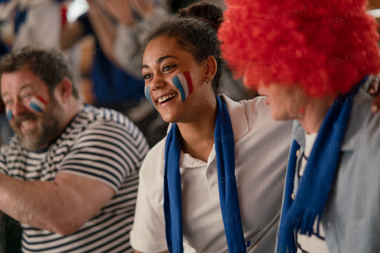 Excited football fans supproting French national team in live soccer match at a stadium.