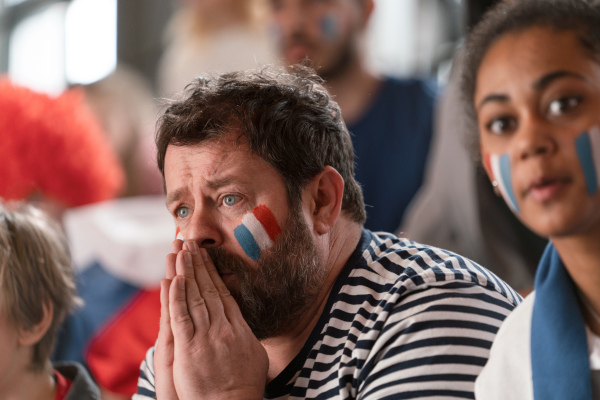 Worried football fans supproting a French national team in live soccer match at stadium.