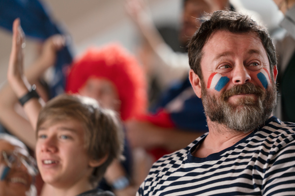 Excited football fans supproting French national team in live soccer match at astadium.