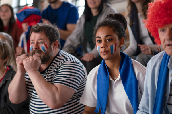 Worried football fans supproting a French national team in live soccer match at stadium.