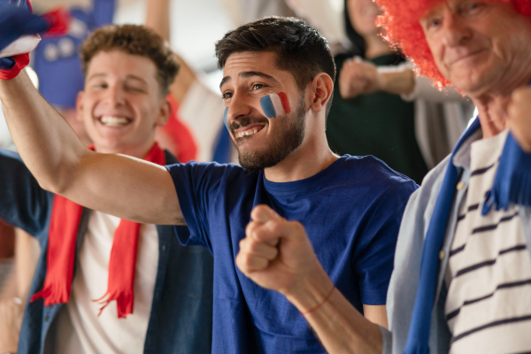 Excited football fans supproting French national team in live soccer match at astadium.