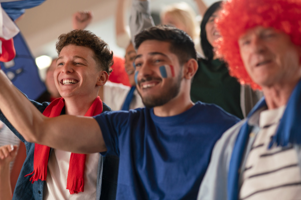 Excited football fans supproting French national team in live soccer match at astadium.