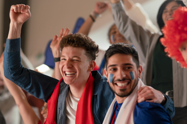 Excited football fans supproting French national team in live soccer match at astadium.