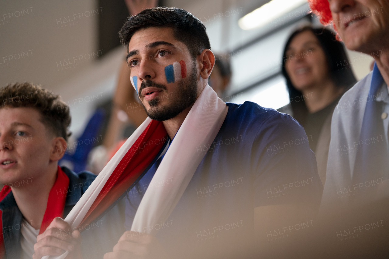 Worried football fans supproting a French national team in live soccer match at stadium.