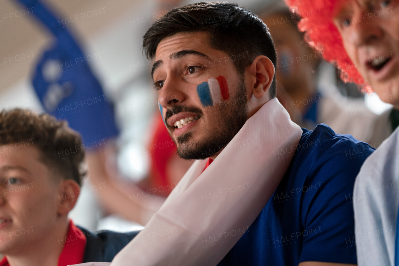 Excited football fans supproting French national team in live soccer match at astadium.