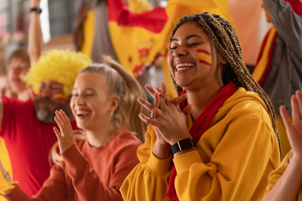 Excited football fans supproting a spanish national team in live soccer match at stadium.