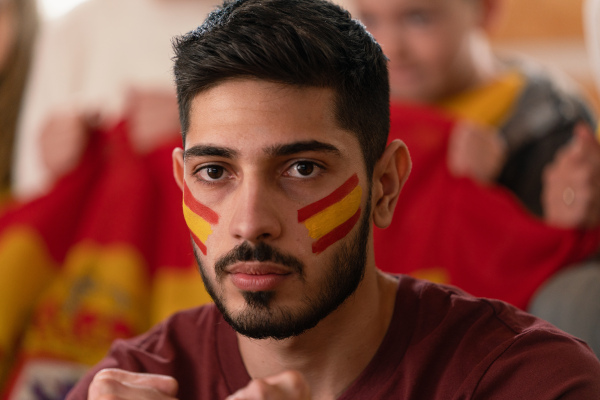 Excited football fans supproting a spanish national team in live soccer match at stadium.