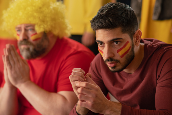 Excited football fans supproting a spanish national team in live soccer match at stadium.