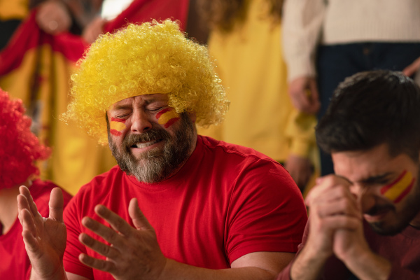 Worried football fans supproting a spanish national team in live soccer match at stadium.