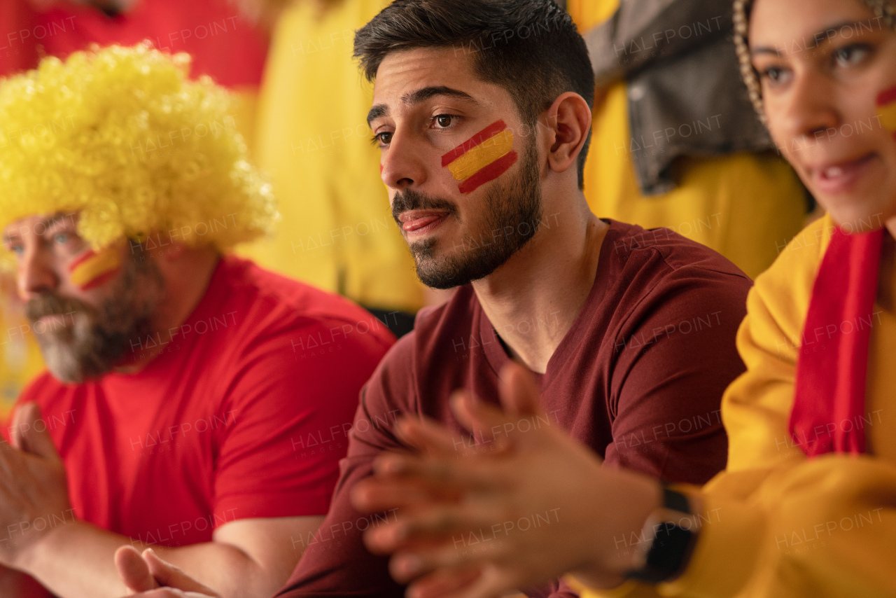 Worried football fans supporting a spanish national team in live soccer match at stadium.