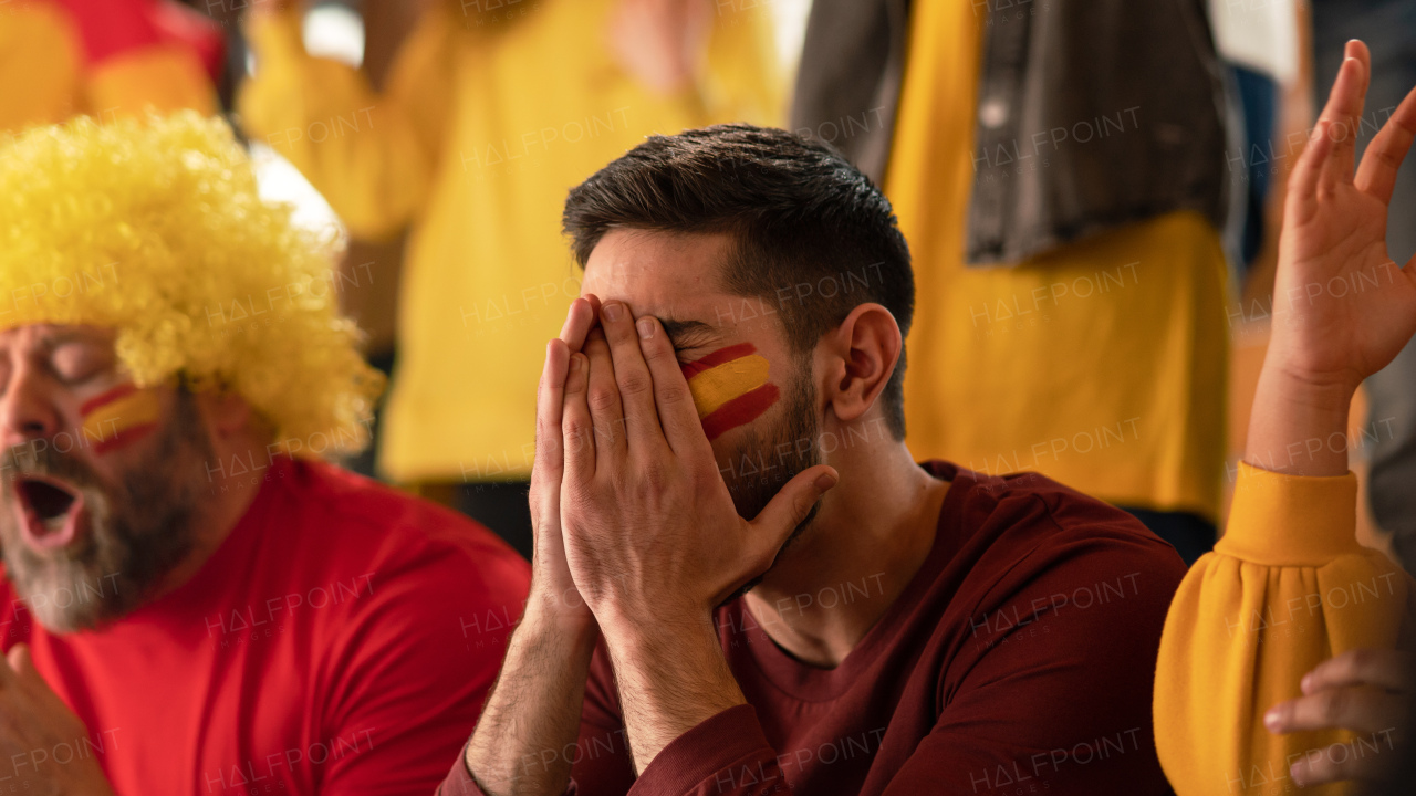 Worried football fans supporting a spanish national team in live soccer match at stadium.