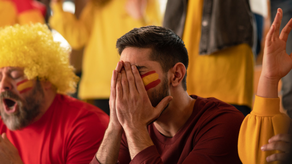 Worried football fans supporting a spanish national team in live soccer match at stadium.