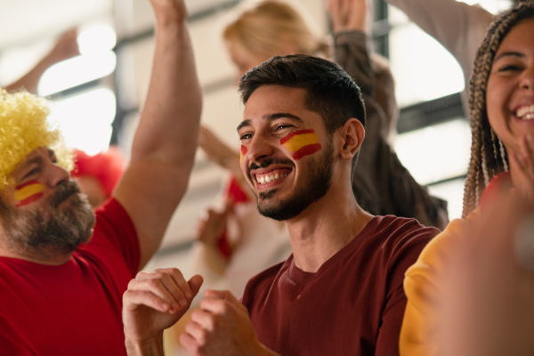 Excited football fans supproting a spanish national team in live soccer match at stadium.