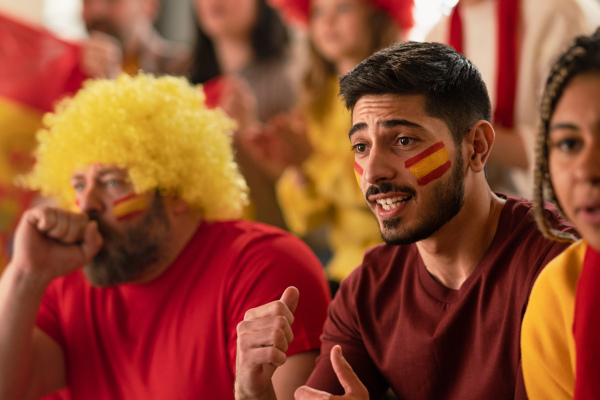 Nervous football fans supproting spanish national team in live soccer match at a stadium.