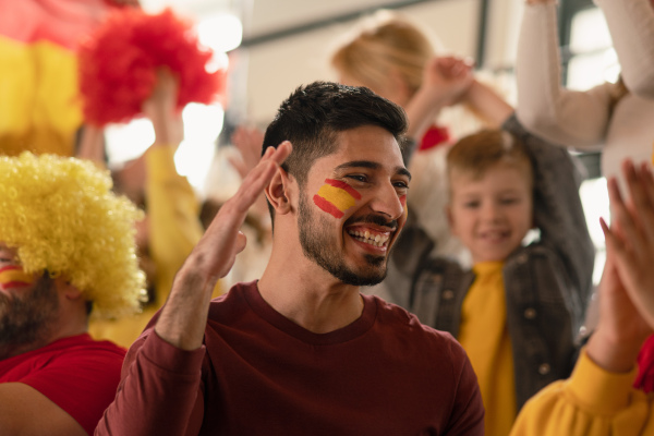 Excited football fans supproting a spanish national team in live soccer match at stadium.