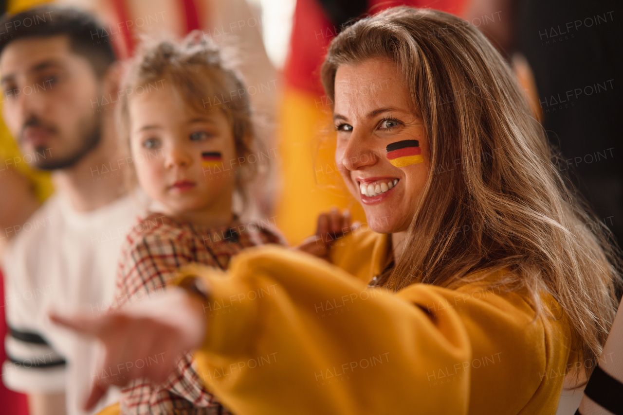 Excited football fans, mother with little daughter, supproting a German national team in live soccer match at stadium.