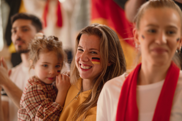 Excited football fans, mother with little daughter, supproting a German national team in live soccer match at stadium.