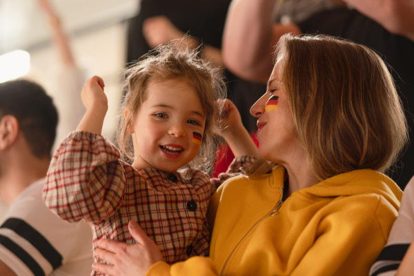 Excited football fans, mother with little daughter, supproting a German national team in live soccer match at stadium.