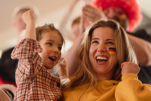 Excited football fans, mother with little daughter, supproting a German national team in live soccer match at stadium.