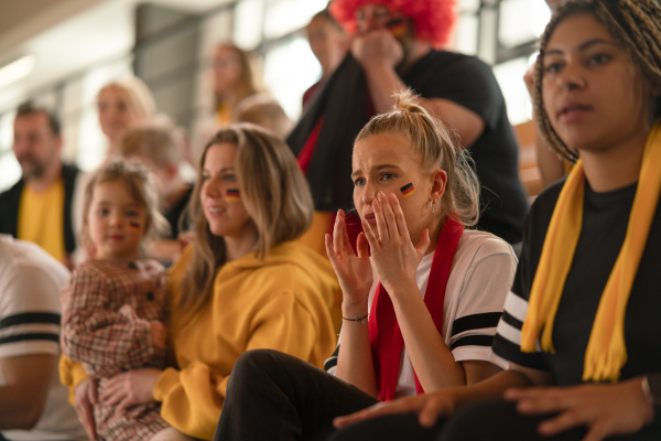 Worried football fans supproting a German national team in live soccer match at stadium.