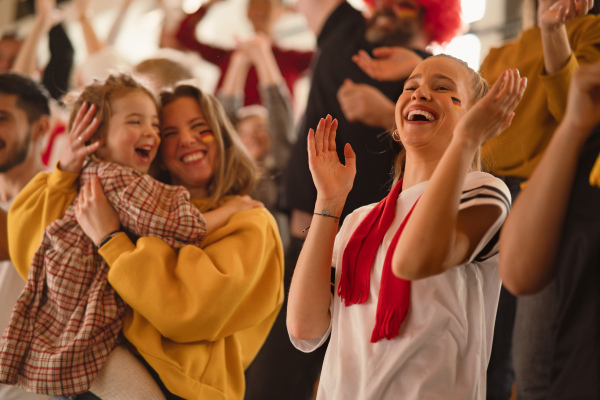 Excited football fans, supproting a German national team in live soccer match at stadium.