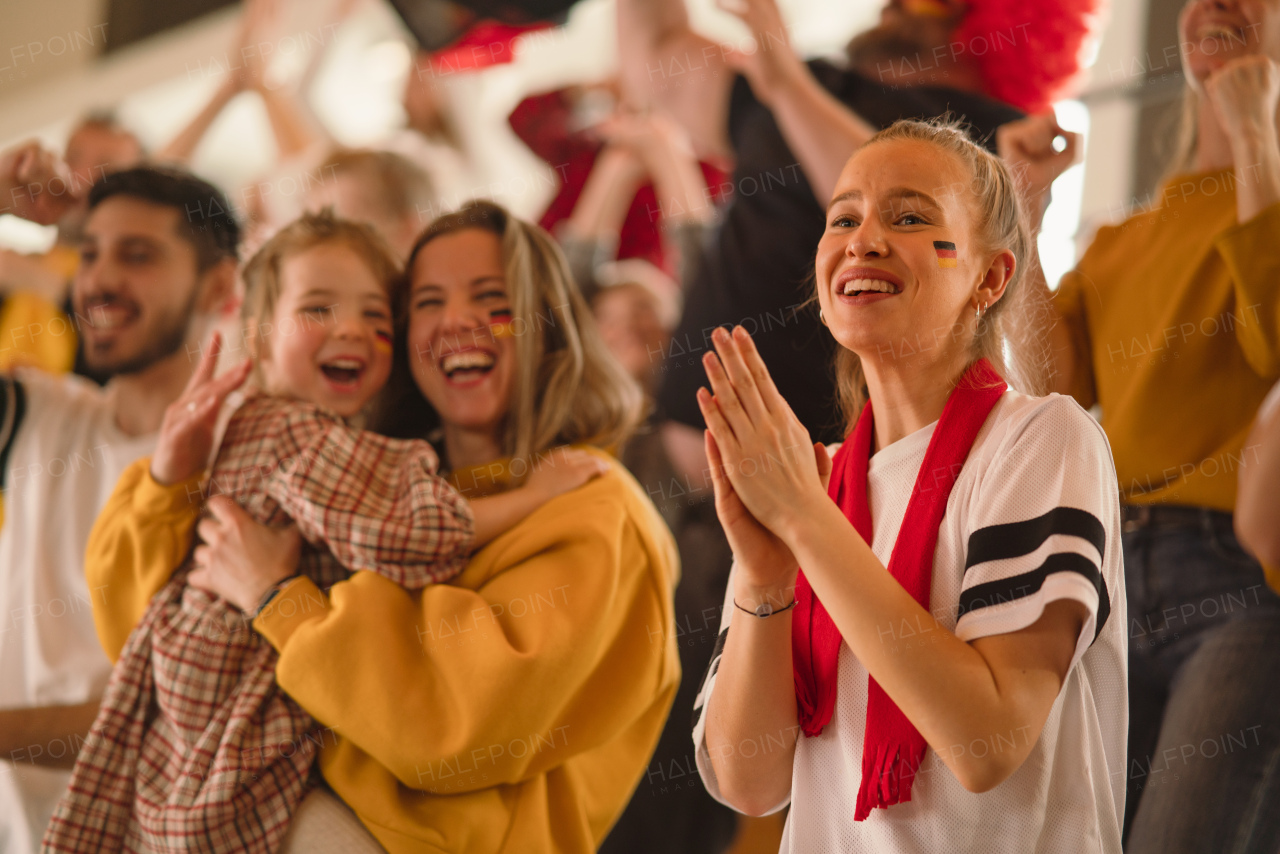 Excited football fans, mother with little daughter, supproting a German national team in live soccer match at stadium.